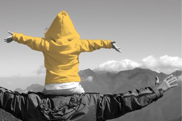 Kind mit gelber Jacke auf Papas Schultern in den Bergen